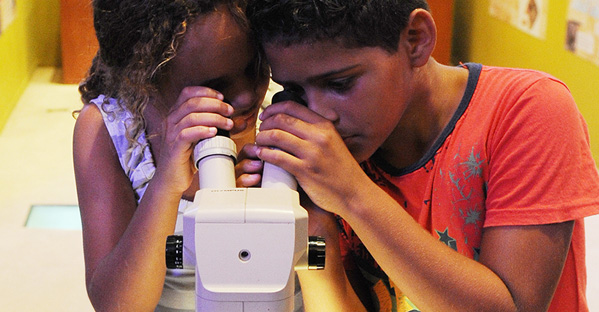 Duas crianças olhando através das lentes de um microscópio