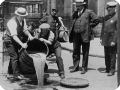 Homens despejam bebida de um barril dentro de um bueiro.