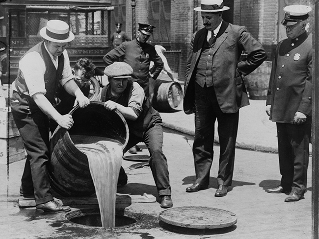 Homens despejam bebida de um barril dentro de um bueiro.