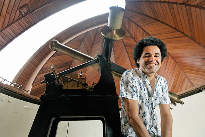 Astrofísico Alan Alves Brito está sorrindo ao lado de equipamento de observação 